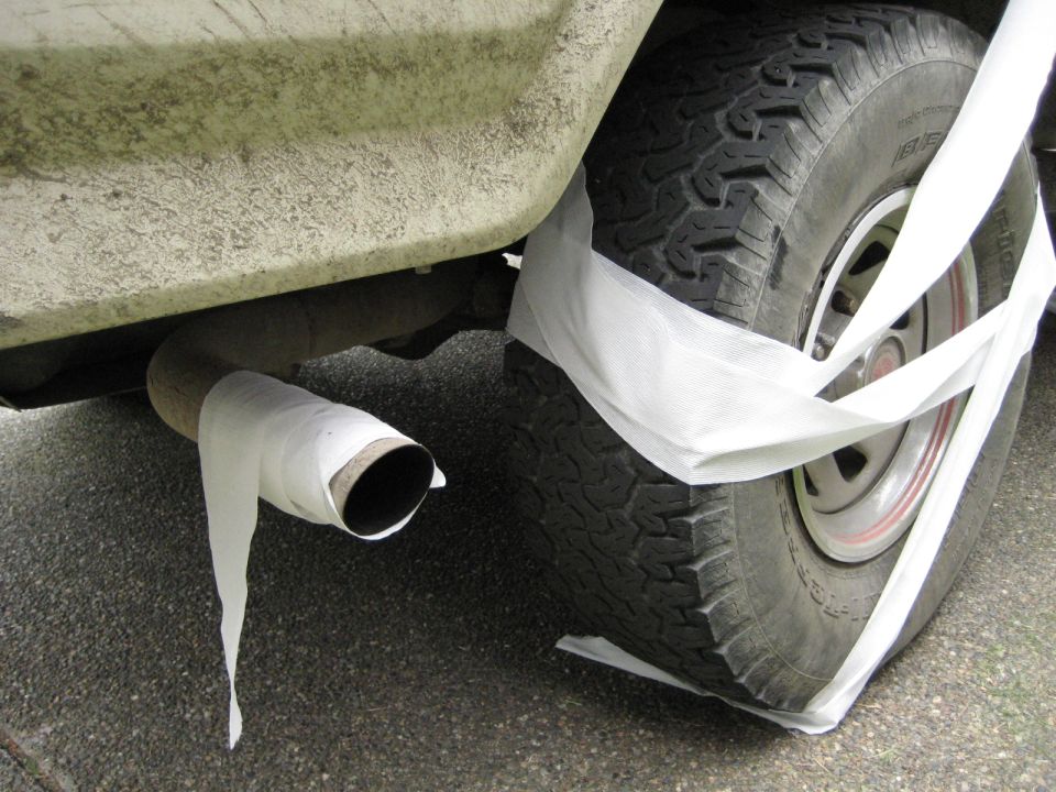 Vehicle rear tire and exhaust pipe wrapped in white tape.