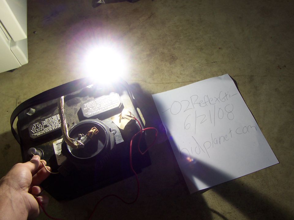 Hand connecting wire to car battery powering a bright light, with a note beside it.