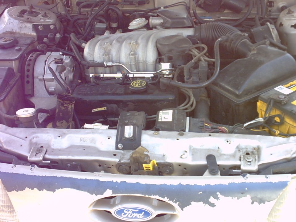 Open hood of a Ford Taurus showing 3.0 V6 engine, air box, battery, and blue front panel with Ford emblem