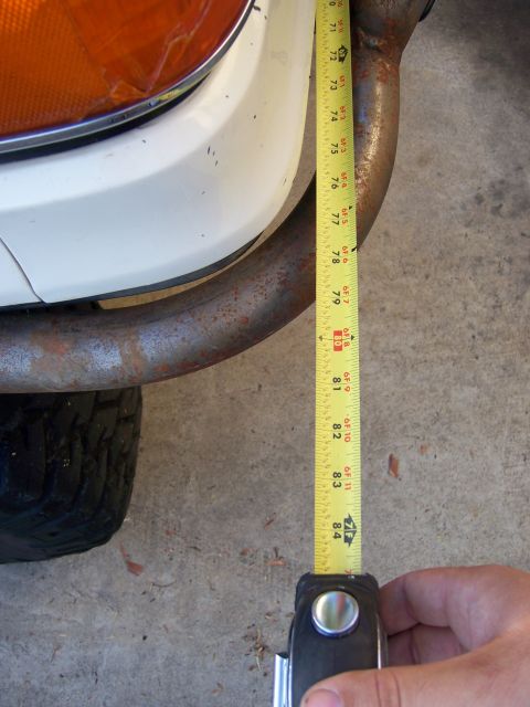 1991 Ford Bronco - Photograph of a tape measure extended vertically alongside a rusty tube bumper at a vehicle's front corner.