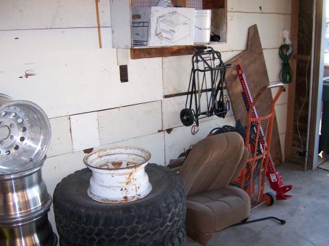 1991 Ford Bronco - Photograph of a garage corner cluttered with wheels, tires, a hand truck and a vehicle seat.