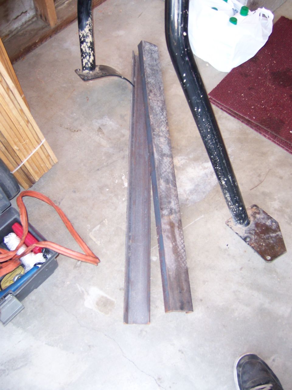Two lengths of fabricated steel channel on a garage floor near a roll cage tube