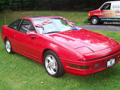 1989 Ford Probe - A bright red 1989 Ford Probe is parked on a grassy lawn with a van in the background. The car's hood and windshield have cleaning cloths an…