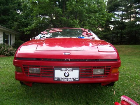 1989 Ford Probe - The front view of a red 1989 Ford Probe is shown parked on a grassy lawn in front of a house and trees. A license plate with text and a BMW…