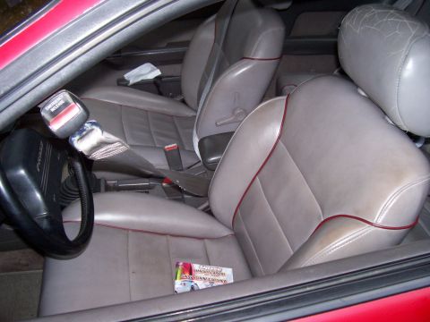 1989 Ford Probe - The interior of a red car, likely a 1989 Ford Probe, is shown with a focus on the driver's side seat and dashboard. The light gray leather…
