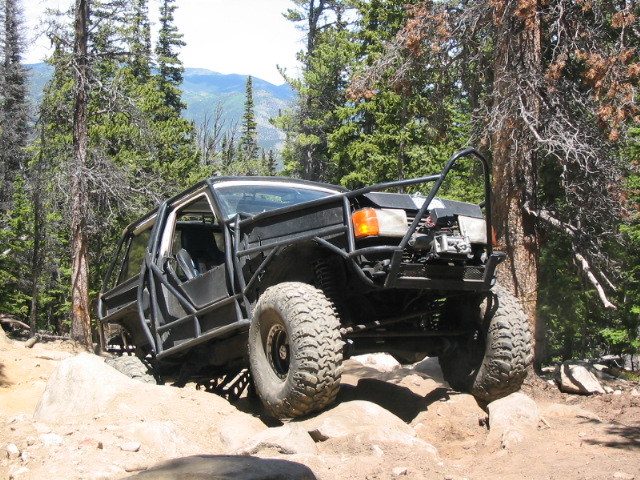 Black tube-caged Ford Bronco rock crawler climbing a boulder on a mountain trail