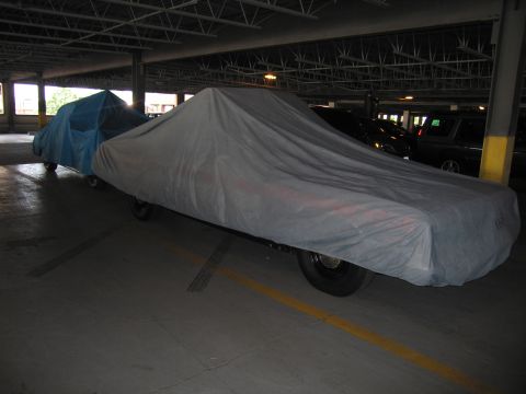 1991 Ford LTD Crown Victoria - Two vehicles draped in gray and blue fabric car covers sit in a covered parking garage.