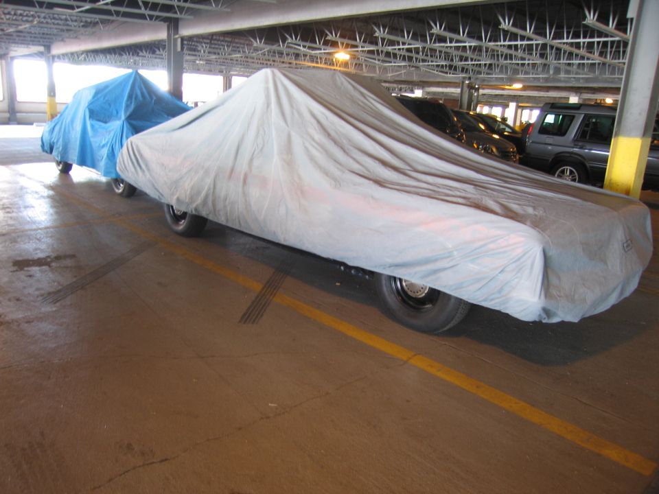 Covered sedan under gray car cover beside a blue-covered vehicle in a garage