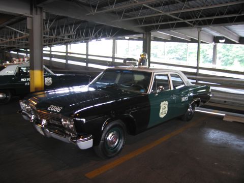 1991 Ford LTD Crown Victoria - vintage green-and-white police sedan numbered 2066 and marked 18 PCT sits with other patrol cars in a covered garage.