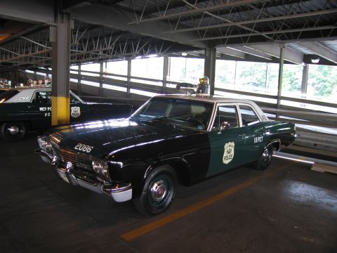 1991 Ford LTD Crown Victoria - Front three-quarter view of a vintage green-and-white police sedan numbered 2066, marked 18 PCT, parked indoors.