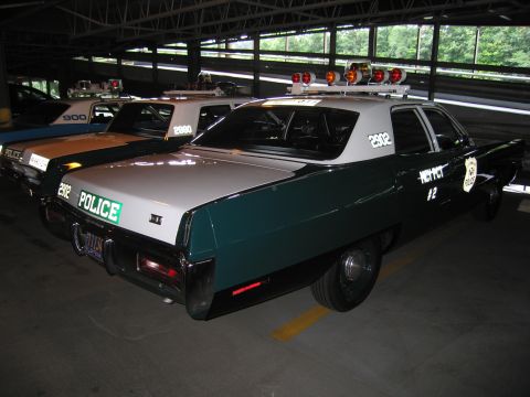 1991 Ford LTD Crown Victoria - Rear three-quarter view of a green-and-white POLICE sedan numbered 2902, marked MCY PCT 2, with roof light bar, parked indoors.