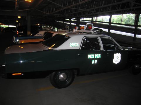 1991 Ford LTD Crown Victoria - Side view of a green-and-white police sedan numbered 2902 and marked MCY PCT 2, lit by garage lights.