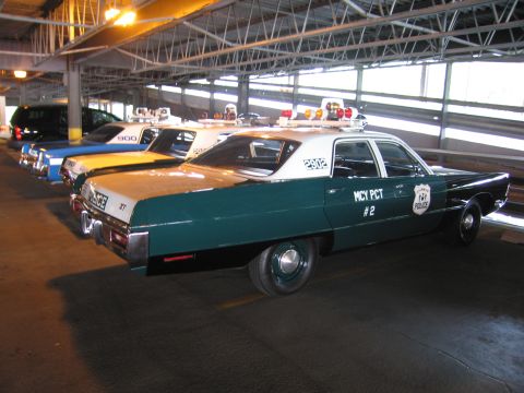 1991 Ford LTD Crown Victoria - Rear three-quarter view of a green-and-white police sedan numbered 2902, marked MCY PCT 2, in a row of patrol cars indoors.