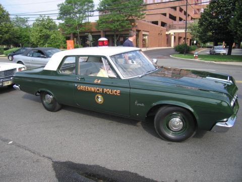 1991 Ford LTD Crown Victoria - green-and-white Plymouth two-door marked GREENWICH POLICE and numbered 64, with a red roof beacon, parked on a street.