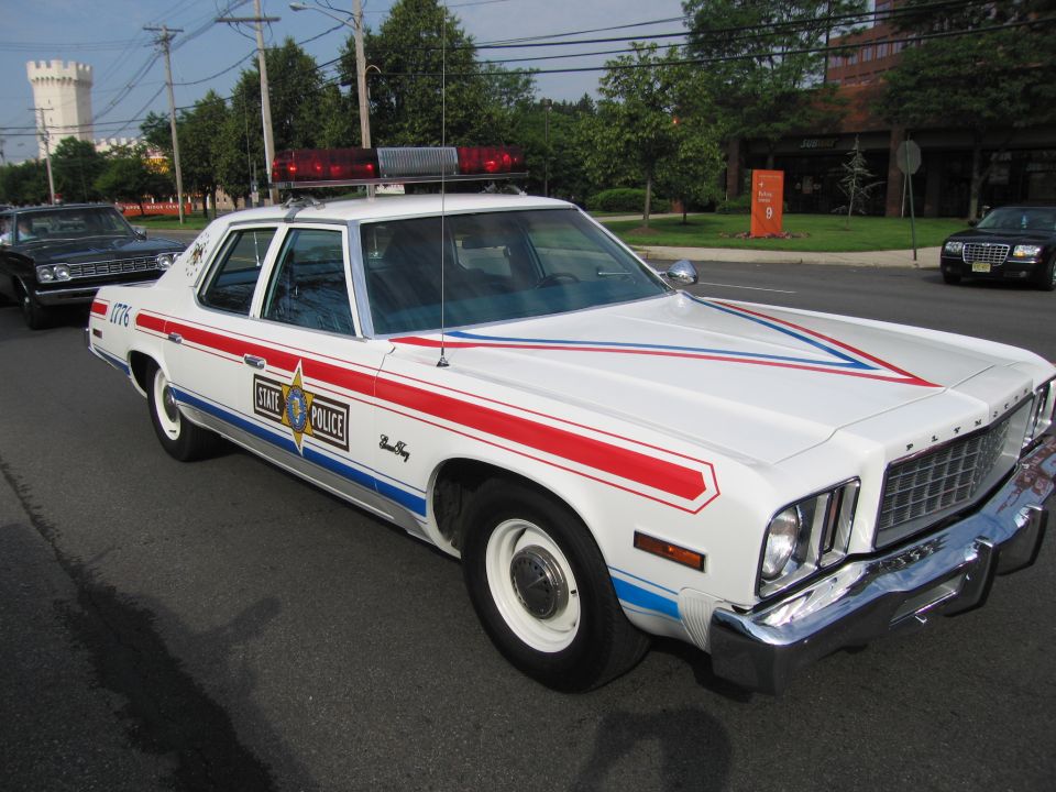 White Plymouth STATE POLICE sedan with red and blue stripes and roof light bar