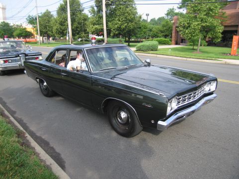 1991 Ford LTD Crown Victoria - dark green vintage four-door sedan with a single red roof beacon and a driver inside, moving along a tree-lined street.