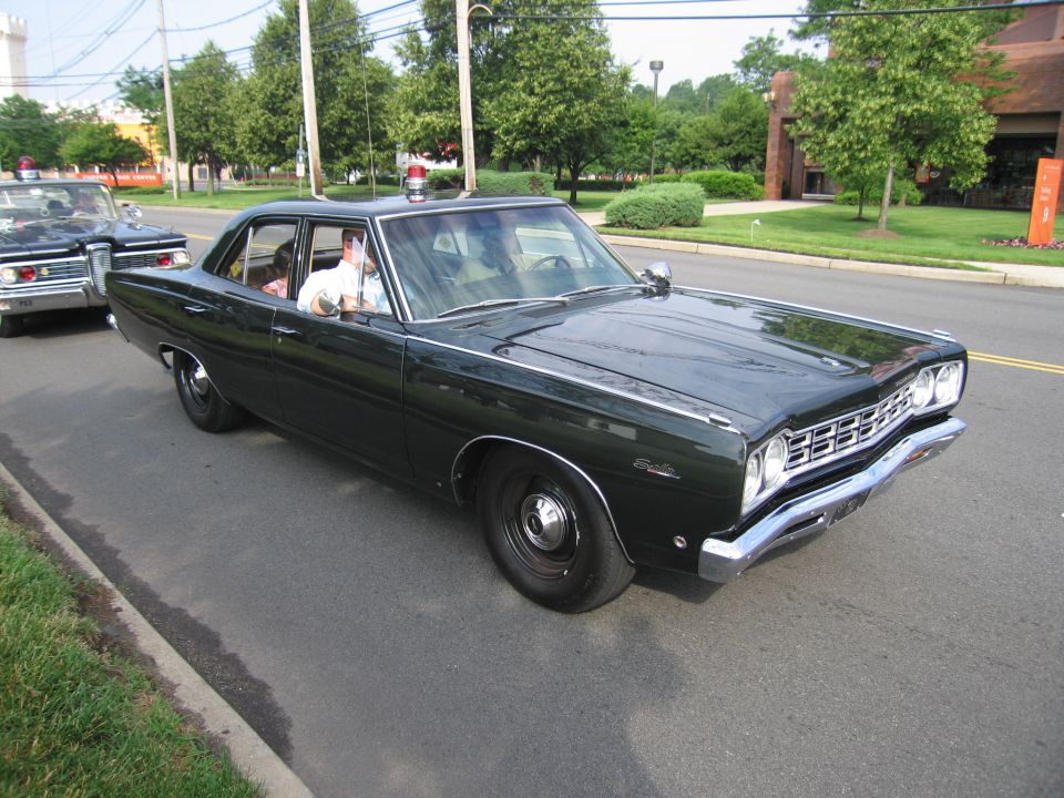 Dark green vintage four-door sedan with roof beacon driving on a street