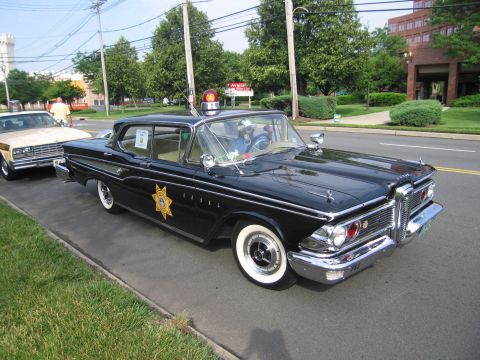1991 Ford LTD Crown Victoria - black late-1950s Edsel four-door sedan bearing a gold police star emblem on the door, with whitewall tires, parked by a curb.