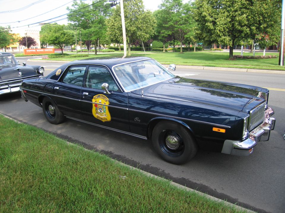 Black 1970s four-door police sedan with gold state-police door shield and roof light