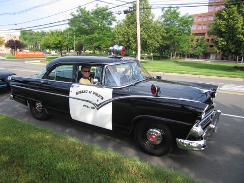 1991 Ford LTD Crown Victoria - black-and-white 1955 Ford four-door police car lettered Bureau of Police, Wilmington Del., with roof siren and spotlights, parked by a lawn.