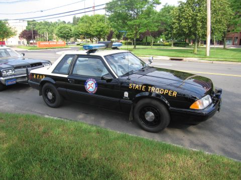 1991 Ford LTD Crown Victoria - black Fox-body Ford Mustang coupe lettered STATE TROOPER and FHP with a Florida Highway Patrol door seal and roof lightbar.