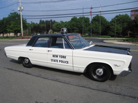 1991 Ford LTD Crown Victoria - white mid-1960s four-door sedan lettered NEW YORK STATE POLICE in black, with black roof and single red roof beacon, parked roadside.