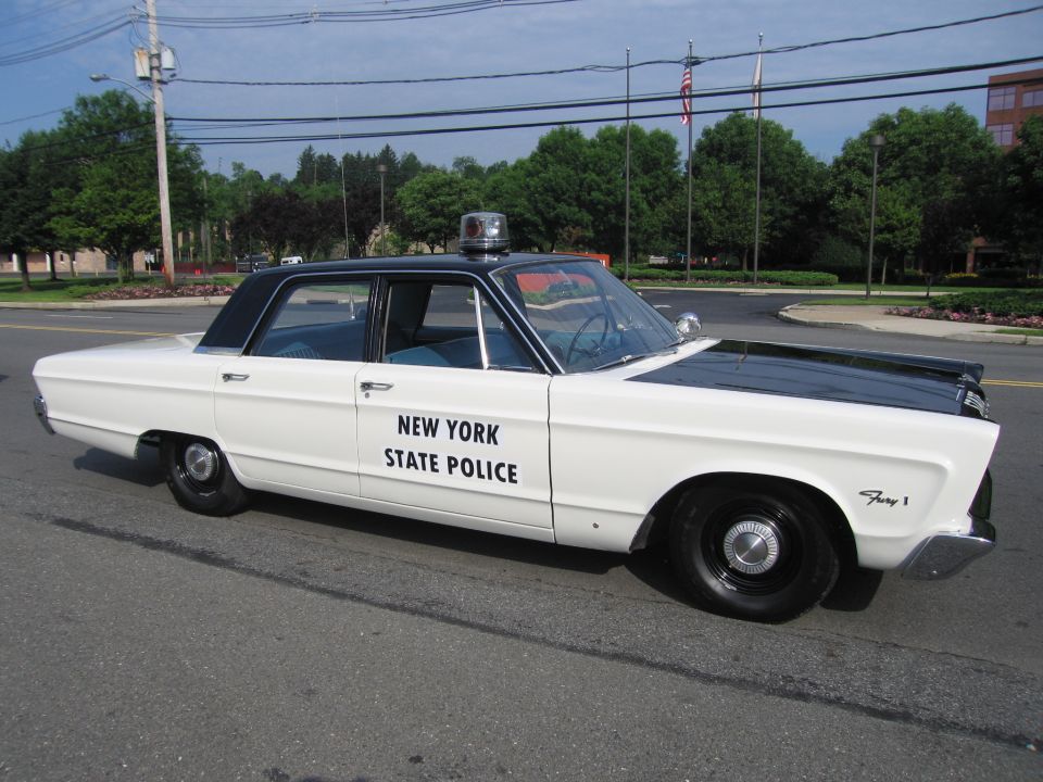 White mid-1960s sedan lettered NEW YORK STATE POLICE with roof beacon