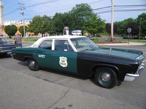 1991 Ford LTD Crown Victoria - green-and-white mid-1960s four-door police car lettered POLICE and 18 PCT with a silver door shield and roof beacon, parked curbside.