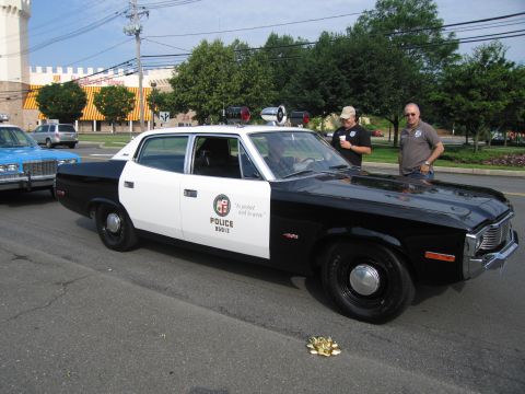 1991 Ford LTD Crown Victoria - black-and-white early-1970s AMC Matador-style police sedan lettered POLICE with an LAPD city seal, roof lights, two men standing behind it.