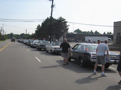 1991 Ford LTD Crown Victoria - long row of vintage police sedans parked along a roadside as several people in casual clothes stand among the cars.