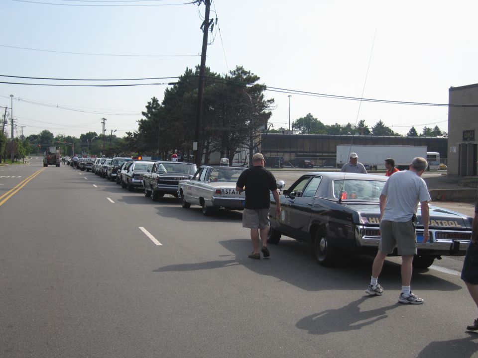 Row of vintage police cars parked along a road with people standing between them