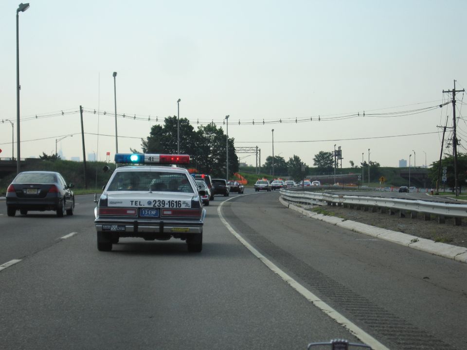 White cruiser marked TEL. 239-1616 driving on a highway with blue roof light lit