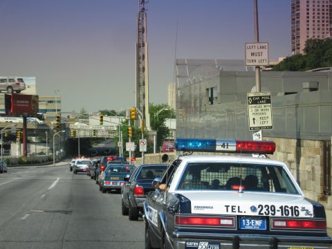 1991 Ford LTD Crown Victoria - line of police cars on a city street with a LEFT LANE MUST TURN LEFT sign; the nearest white cruiser is lettered TEL. 239-1616.