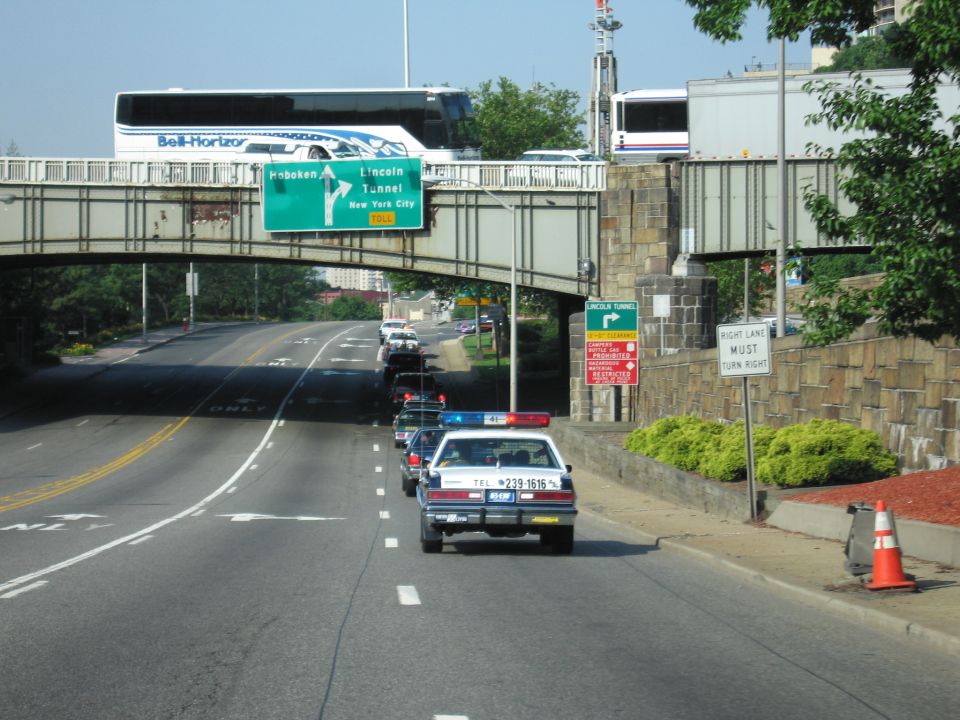 White police cruiser on a road approaching an overpass with Lincoln Tunnel signs