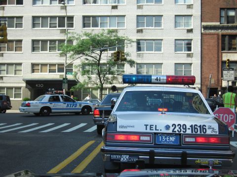 1991 Ford LTD Crown Victoria - white police cruiser lettered TEL. 239-1616 at a city intersection beside an NYPD cruiser and a STOP sign, apartment building behind.