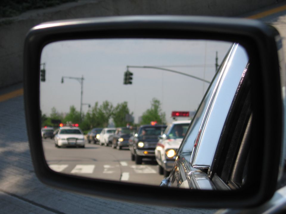 Side mirror reflection of a line of cars including police-style vehicles on a city street