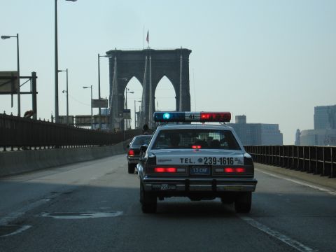 1991 Ford LTD Crown Victoria - black-and-white police-style sedan marked TEL. 239-1616 crosses the Brooklyn Bridge toward the Manhattan skyline.
