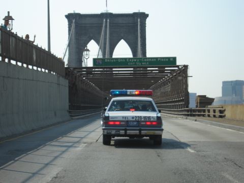 1991 Ford LTD Crown Victoria - police-style sedan crosses the Brooklyn Bridge, passing a green Bklyn-Qns Expwy Cadman Plaza W exit sign.