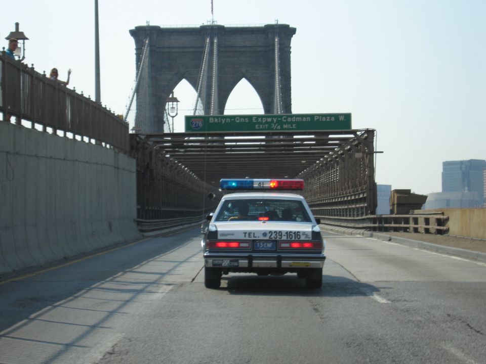 Police-style sedan on Brooklyn Bridge passing a Bklyn-Qns Expwy exit sign