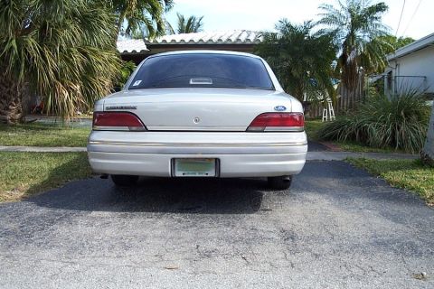 1992 Ford Crown Victoria - Rear view of a silver 1992 Ford Crown Victoria sedan parked in a driveway with palm trees and a house in the background.