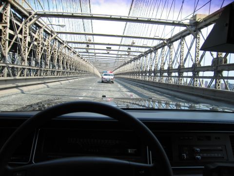 1991 Ford LTD Crown Victoria - Seen over a dashboard and steering wheel, a police-style sedan drives ahead on a steel suspension bridge roadway.