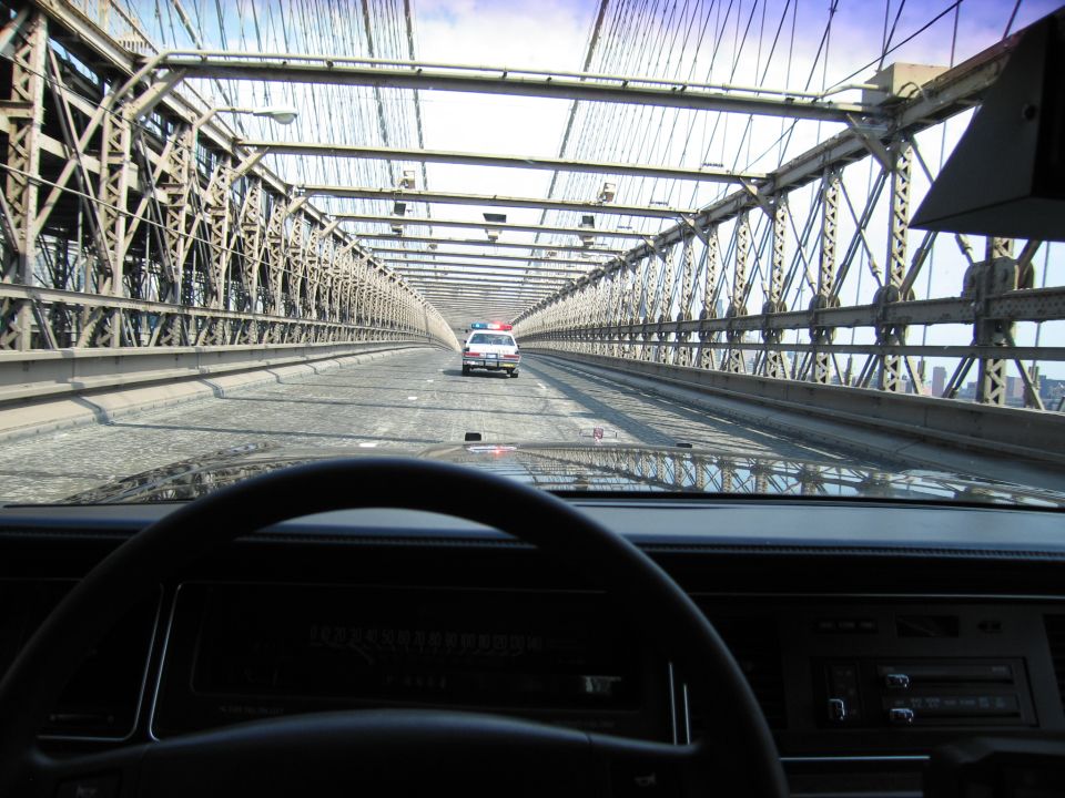 Dashboard view of a police-style car ahead on a steel suspension bridge roadway
