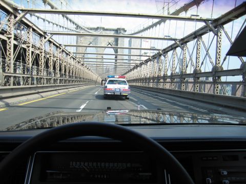 1991 Ford LTD Crown Victoria - From a car interior, a police-style sedan drives ahead across the Brooklyn Bridge framed by cables and stone towers.