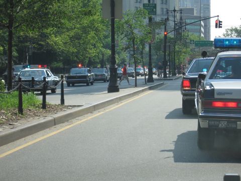 1991 Ford LTD Crown Victoria - black-and-white police-style sedan drives a tree-lined city boulevard as a pedestrian crosses and other cars approach in the far lanes.