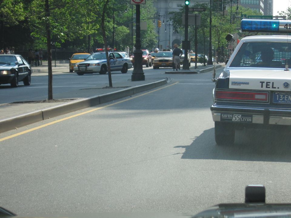 Police-style sedan on city street with an NYPD Crown Victoria and yellow taxi across the median