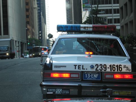 1991 Ford LTD Crown Victoria - police cruiser with light bar, Connecticut 13-ENF plate and SAVES 55 LIVES bumper sticker drives down a city street at dusk.