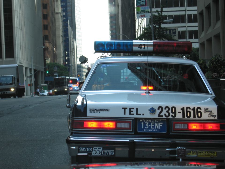 Rear of police sedan TEL. 239-1616, SAVES 55 LIVES bumper, city street