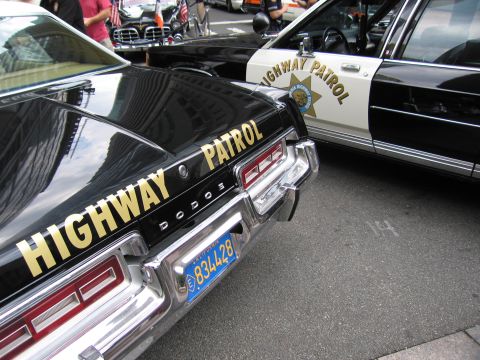 1991 Ford LTD Crown Victoria - Close view of a black Dodge HIGHWAY PATROL car rear and plate, parked next to a black-and-white California Highway Patrol cruiser.