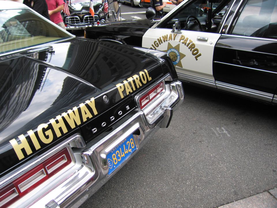 Rear of black Dodge Highway Patrol car with blue California plate beside CHP cruiser