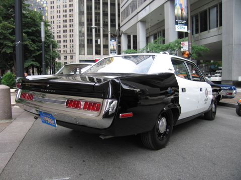 1991 Ford LTD Crown Victoria - black-and-white AMC Matador police sedan parked along a downtown sidewalk, shown from the rear three-quarter angle.